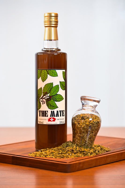 THE MATE bottle 700ml standing on a wooden cupboard with some yerba mate next to it